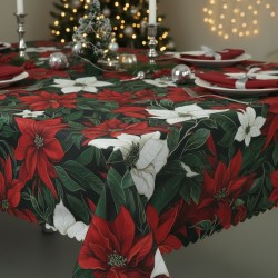 Obrus świąteczny z wzorem w czerwone kwiaty Gwiazdy Betlejemskiej i zielony ostrokrzew. Brzegi wykończone ząbkiem. Obrus jest wyeksponowany na zastawionym stole.