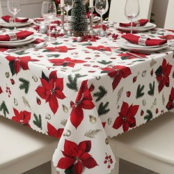 Obrus świąteczny z wzorem w czerwone Poinsecje, igliwie i bombki na jasnym tle. Brzegi wykończone ząbkiem. Obrus jest wyeksponowany na zastawionym stole.